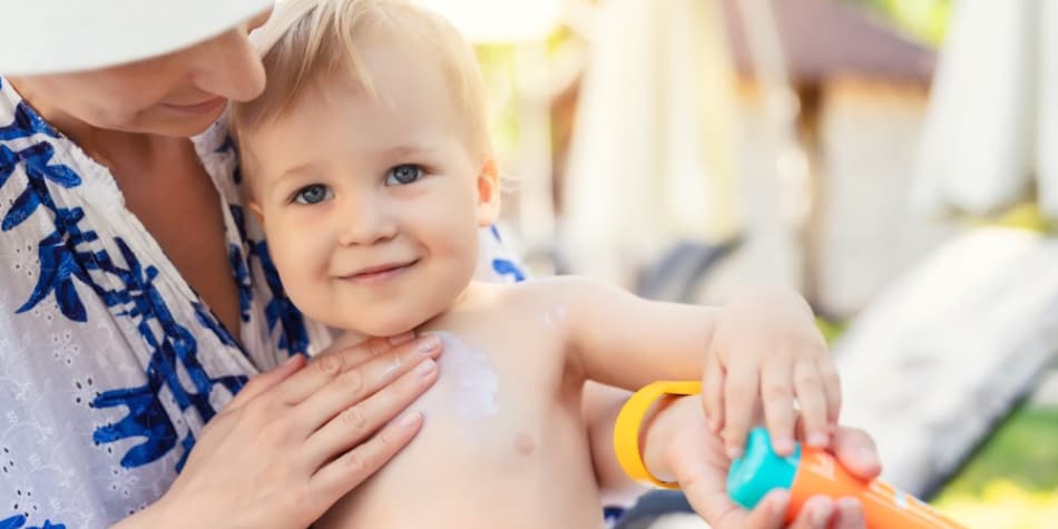 A mom applies sunscreen to her toddler
    son outside.